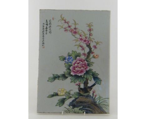 A Chinese ceramic panel with enamel painting in the famille rose palette of a bird on a branch with flowers. Character writin