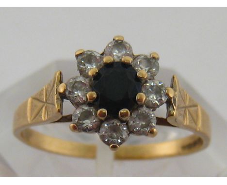 A 9 carat yellow gold, sapphire and white stone cluster ring, the central dark sapphire 5mm diameter, finger size R, 2.4 gms 