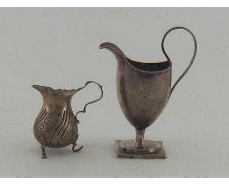 A late Victorian embossed silver cream jug on three feet in the George II manner, Deykin and Harrison, Birmingham, 1899, toge
