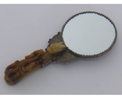 A Chinese hand mirror mounted in white metal embossed with a dragon , the handle a jade belt buckle carved as a mythical beas