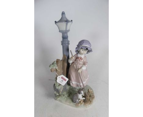 A large Lladro Spanish porcelain figure modelled as a girl beside a lamppost and fence, sweeping leaves with a cat before her
