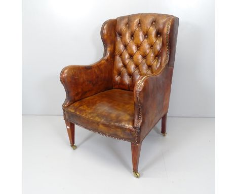 An Edwardian button back brown leather-upholstered wingback fireside arm chair. 