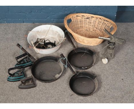 A selection of metal items including Swain graduated cast iron pans and irons in a enamel bowl and wicker basket.  