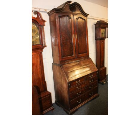 A George III mahogany bureau bookcase with broken arch surmount, two panelled doors enclosing shelves, pigeon holes and small