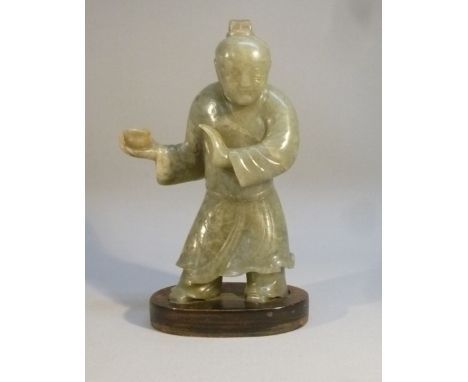 A CHINESE GREEN MOTTLED JADE FIGURE OF A MAN HOLDING A CUP IN HIS RIGHT HAND WEARING A DECORATED ROBE STANDING ON A LATER BAS