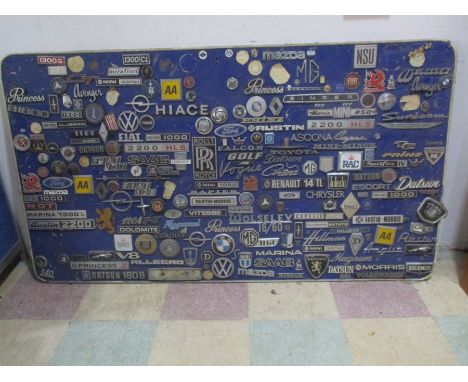 A large collection of vintage car badges mounted on a board, including Rolls Royce, Ford, BMW, Mazda, AA, Chrysler, SAAB, etc