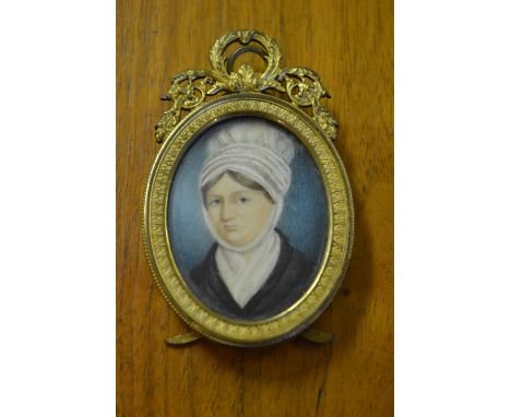 19th Century oval head and shoulder portrait miniature, lady in a white bonnet, housed in a gilt brass oval frame with floral