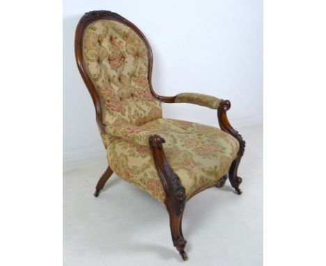 A Victorian nursing chair, the walnut frame carved with roses and scrolls, upholstered in button back floral beige fabric, ra