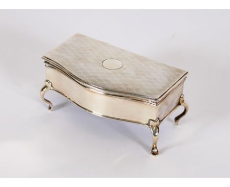 An early 20th Century silver trinket casket, of serpentine shape, the engine turned lid opening to reveal a plush lined inter