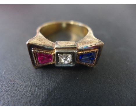 A Continental gilt plated three stone ring in the form of a bow tie set with central diamond flanked by a ruby and a sapphire