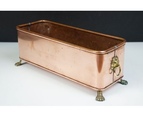 Copper rectangular planter with rolled rim and brass lion mask drop ring handles, raised on brass lion paw feet, 36cm long x 