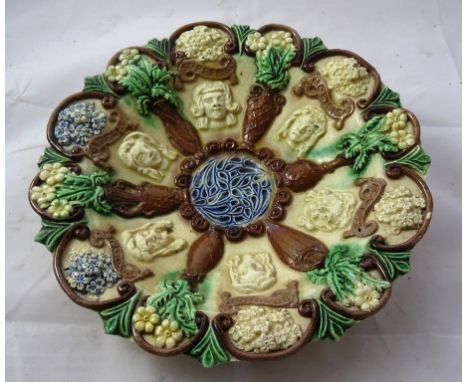 An Edward Bingham for Castle Hedingham pottery Palissy-style plate: Moulded in relief with portrait masks and flower filled u