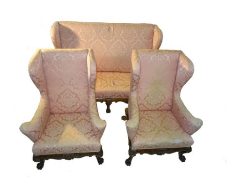 A George II style mahogany two-seater sofa and two wingback chairs: Upholstered in pink floral silk, the shaped aprons and li