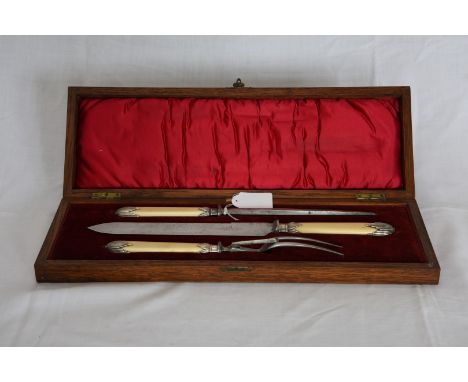 A three piece carving set comprising carving knife, fork and steel with bone handles and gadrooned finials in a red velvet li