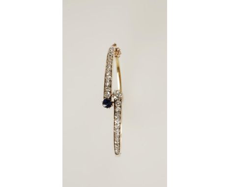 A SAPPHIRE AND DIAMOND CROSSOVER BANGLE, circa 1900, channel and claw-set with tapering circular-cut diamonds, terminating wi