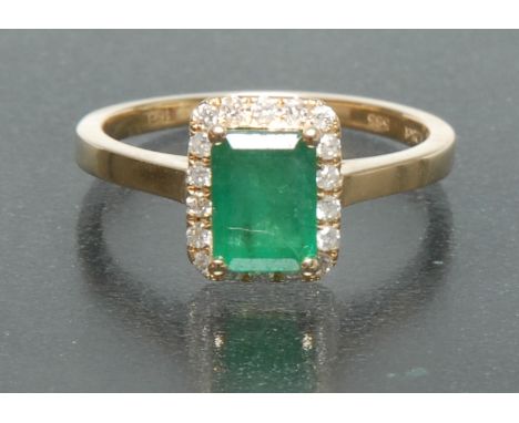 An emerald and diamond ring, central rectangular emerald approx 1.28ct, above a surrounding band of eighteen round brilliant 