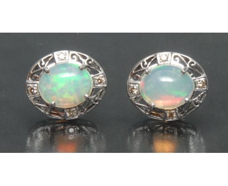 A pair of opal and diamond oval earrings, each with a central oval cabochon opal, flashing green, violet, orange, and red col