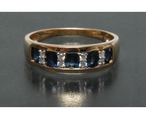 A sapphire and diamond line ring, channel set with five graduated oval blue sapphires each divided by a pair of round brillia