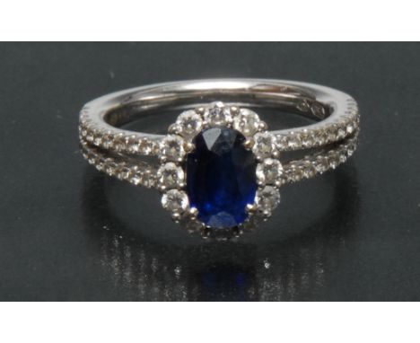 A contemporary sapphire and diamond cluster ring, central oval deep blue sapphire approx 1.07ctm surrounded by a collar of tw