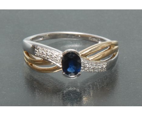 A sapphire and diamond ring, two tone yellow and white gold crossed crest inset with a single oval blue sapphire, approx 0.42