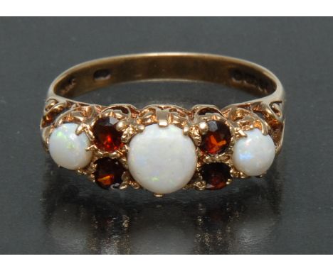 An opal and red garnet ring, central round cabochon opal between a smaller conforming stone either side, each divided by a pa