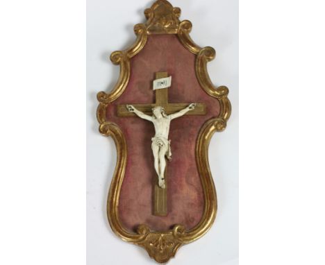 A fine carved ivory Corpus Christi, 19th Century, mounted on a gilt cross in a carved cartouche shaped gilt frame with C scro