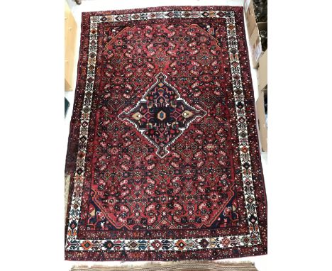 A Persian carpet, the central panel set with diamond shaped medallion on a red ground, with stylised foliate and scrolling de