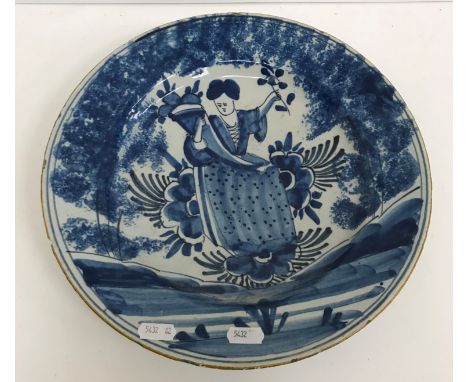 An 18th Century Delft dish, the centrefield decorated with woman in garden setting holding a cornucopia in one arm and a flow