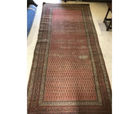 A Persian carpet, the central panel set with repeating hook medallions on a red ground, within a stepped multi-coloured styli