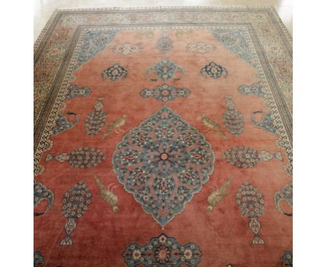 A FINE TABRIZ CARPET, the salmon pink ground worked with a central pale blue and ivory oval floral medallion, birds, stylised