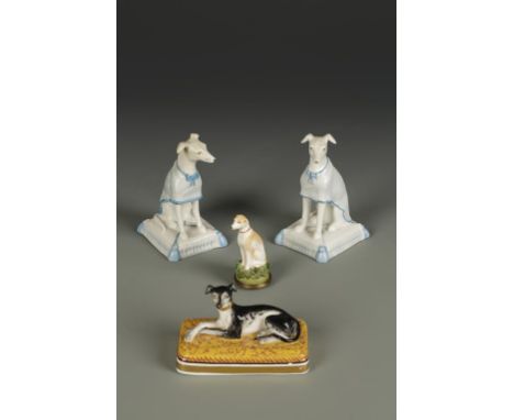 A PAIR OF GERMAN PORCELAIN MODELS OF SEATED WHIPPETS, wearing turquoise lined coats seated on square tasseled cushions, incis