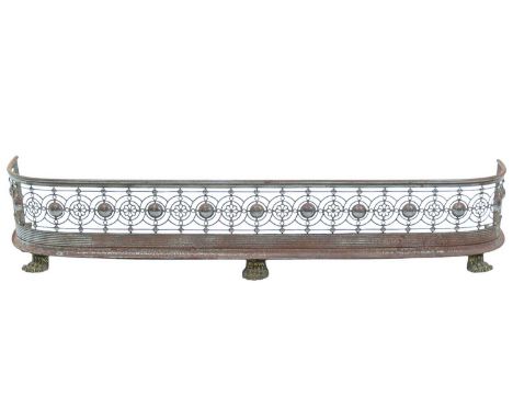 A polished steel fender. Circa 1840, with pierced decoration and raised on brass lion's paw feet, width 121cm.