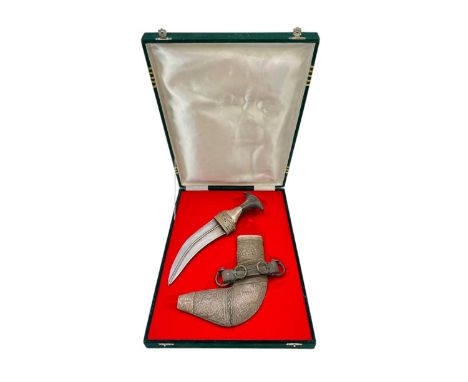 An Omani jambiya dagger and scabbard. The dagger features a horn hilt and a curved blade, with a white metal scabbard with th