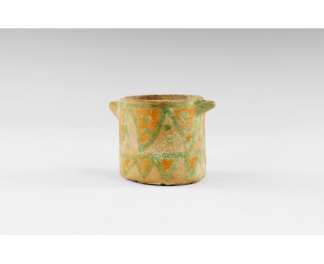 9th-6th century BC. A tubular ceramic pyxis with pierced lug handles to the rim, yellow glazed field with green geometric des