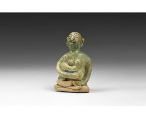 12th-16th century AD. A green-glazed ceramic figurine of a nude seated female suckling a baby in her arms; hollow to the unde