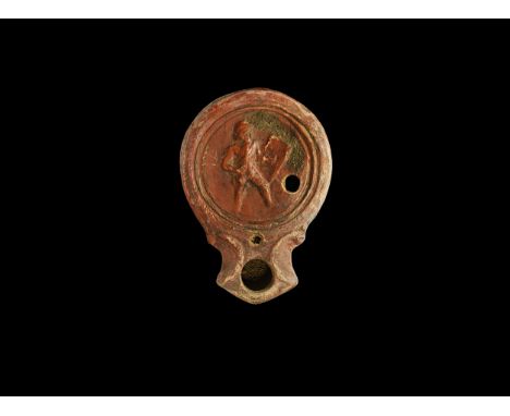 1st century AD. A terracotta lamp with short nozzle and scrolled shoulders, two concentric rings to the discus with high-reli