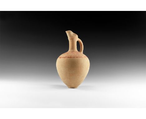 8th-7th century BC. An unglazed ceramic jug with low basal ring, globular body, trumpet-shaped neck with carination and pouri