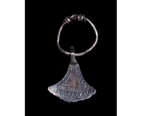 8th-12th century AD. A silver axe-shaped pendant with incised line and triangles to the border; integral suspension loop to t