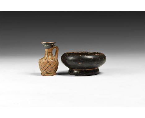 3rd-2nd century AD. A group of two ceramic items comprising of: a miniature jug with painted net motif, a black glazed dish w