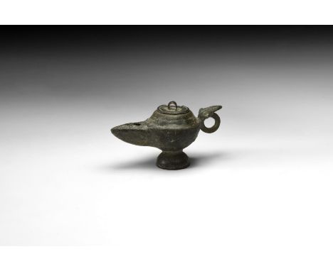 1st-2nd century AD. A miniature bronze oil lamp with discoid base, removable lid, triangular-section nozzle, phallic decorati