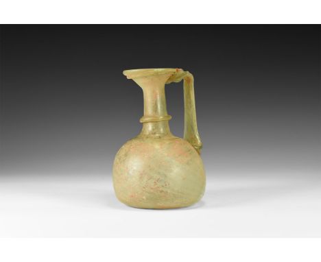 2nd-3rd century AD. A translucent green glass pitcher with bulbous body, pontil base, narrow neck with applied collar, flared
