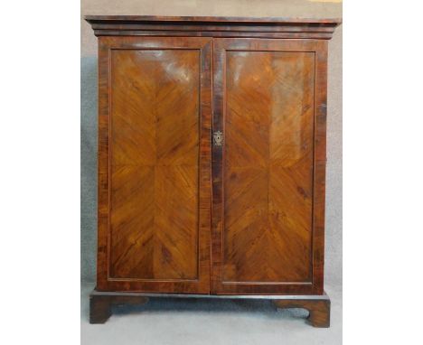 A Georgian mahogany press cupboard with quarter veneered and crossbanded panel doors enclosing shelves and an arrangement of 