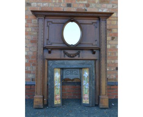 A 20TH CENTURY FIREPLACE, having fancy oak surround, with dentil cornice, insert oval bevelled plate mirror and carved fruit 