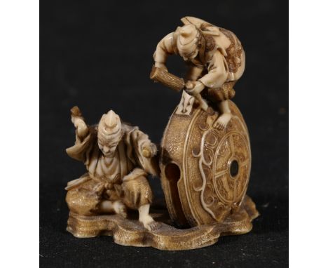 Intricately carved ivory netsuke or okimono depicting two carvers carving an elaborate wheel, decorative base with flower him