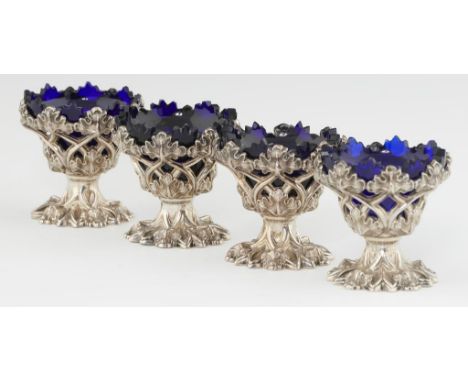 A SET OF FOUR VICTORIAN GOTHIC SILVER OPENWORK SALT CELLARS  blue glass liners, 7cm h, by Henry Wilkinson &amp; Co, Sheffield