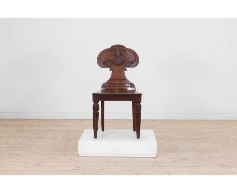 A William IV mahogany hall chair, c.1820s, the waisted back carved with an anthemion to the centre, the plank seat raised on 