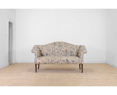 A George III-style mahogany settee, late 19th century, with a camel back, upholstered in floral crewel work fabric, raised on