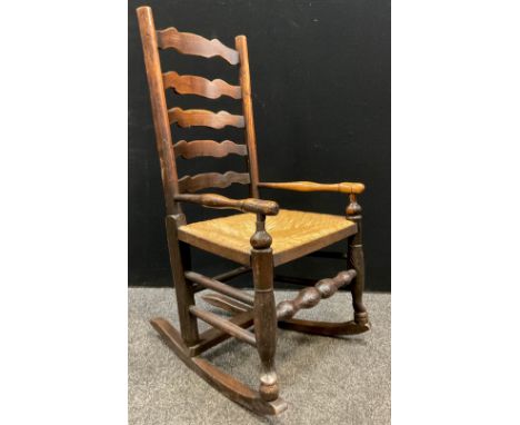 A George III elm ladder-back rocking chair, of small proportions, rush seat, 95.5cm high x 51cm wide x 61cm deep. 