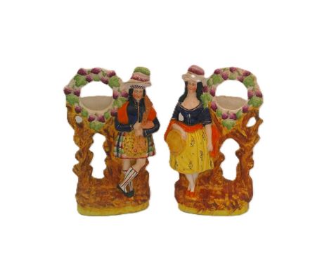 A pair of Staffordshire portrait figures of boy and girl musicians standing along side pocket watch holders, she with a tambo