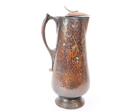 An early 20th century Arts &amp; Crafts hand hammered copper ewer jug. The jug having hinged lid atop, with shaped arrow knop
